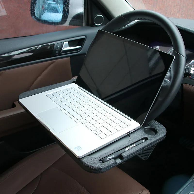 Laptop open on the desk tray clipped to a car steering wheel