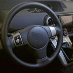 Lace-up leather car steering wheel cover fitted to the wheel, seen from the driver's seat
