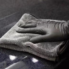 Gloved hand drying dark car paintwork with the microfiber towel