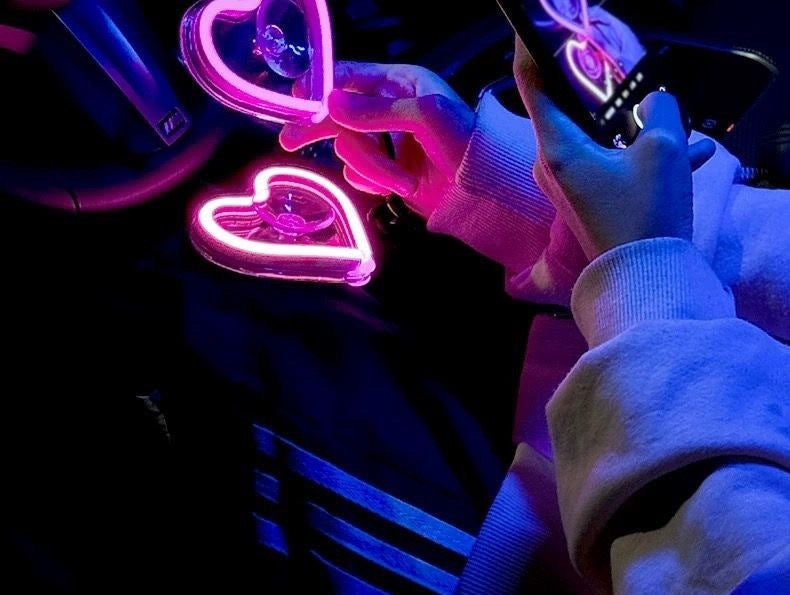 Neon heart lights glowing pink in a car window at night